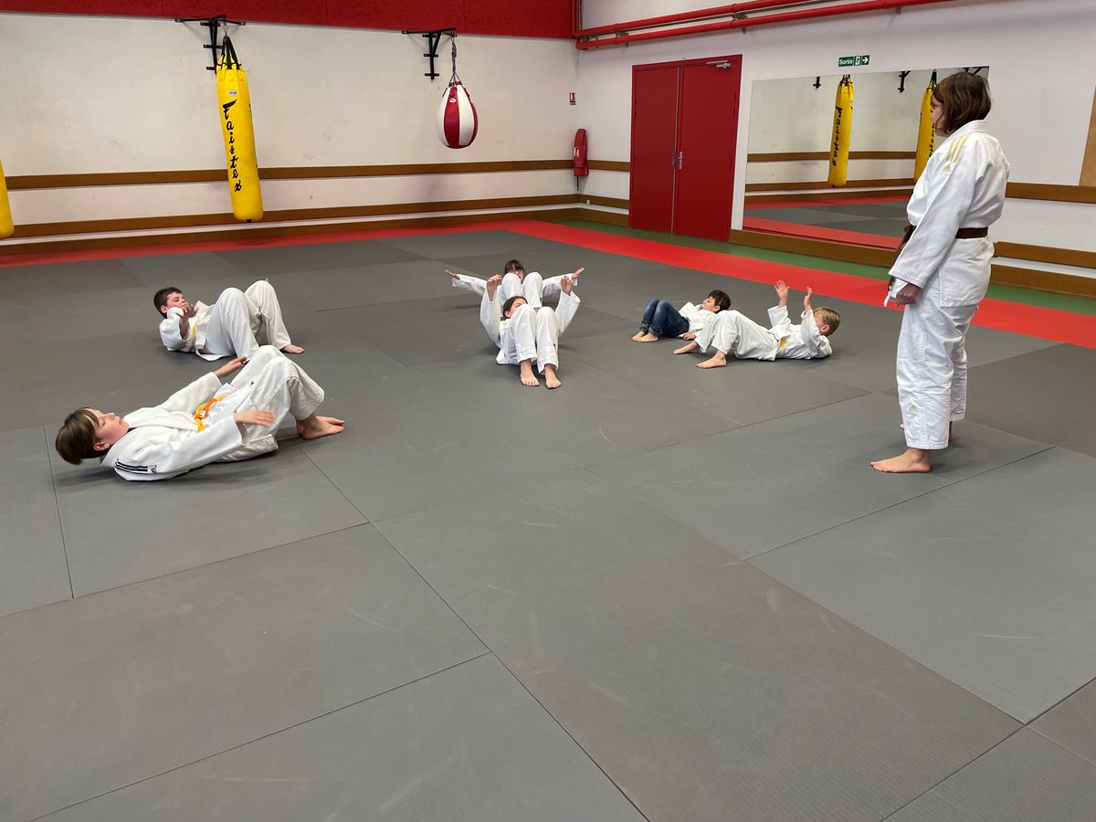 Des enfants font l'échauffement allongés sur le tatami.